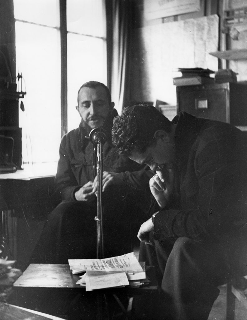 L’abbé Pierre dans son bureau à Neuilly-Plaisance (France), enregistrant une émission pour Radio-Luxembourg (lancement de la campagne des billets de 100 francs), [1954]. © Emmaüs International